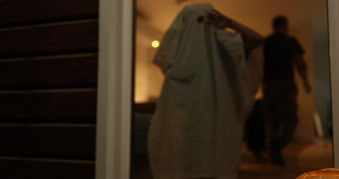 AOn a chilling Halloween night, a ghostly figure of a child in a ghost costume hides in the dark next to a beautifully carved pumpkin, a cute home scene from real life. High quality 4k footage