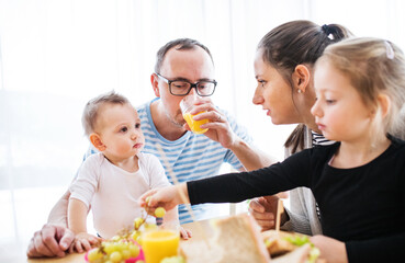 Parents with two children eating a tasty, healthy breakfast in the kitchen. Happy family moment.