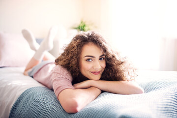 Fototapeta premium Portrait of beautiful young woman with curly hair, lying on stomach on bed.