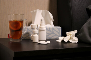 Hot tea with lemon, pills, nose spray, throat spray and on a night table near bed