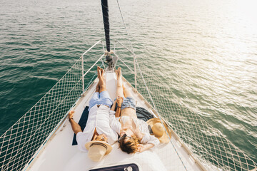 A couple relaxes on the deck of a yacht, enjoying the serene view of the ocean. They are lying side...