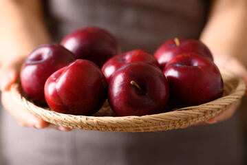 Red plum fruit in basket holding by woman hand, Healthy eating