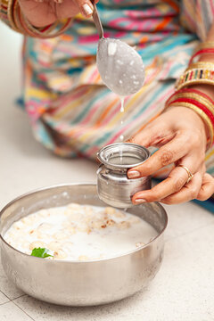 An Indian woman pours panchamrit into a lota, preparing for prasad distribution on the occasion of 'Krishna Janmashtami'.