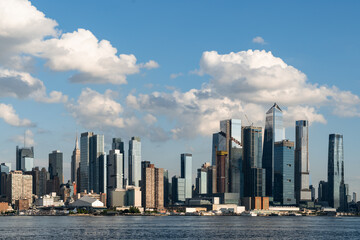 Fototapeta premium New York City skyline with skyscrapers and waterfront under a blue sky with clouds.