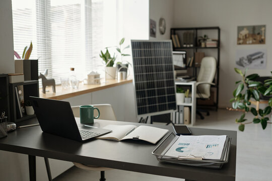 Desk with laptop, open copybook with blank pages and tray with business documents against solar panel mockup