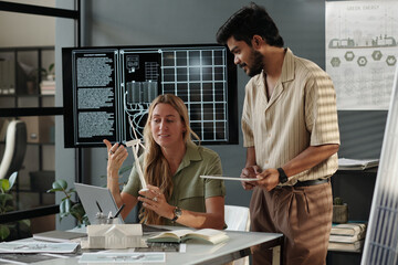 Young businessman with tablet looking at windmill mockup in hands of colleague during project presentation