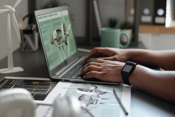 Hands of young unrecognizable businessman pressing keys of laptop with windmill turbine sketch on screen