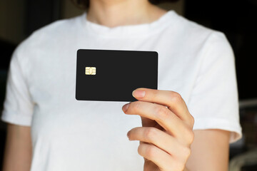White young woman in white t-shirt holding credit or debit black card mockup template. Woman showing bank card, Pay with plastic credit or debit card.