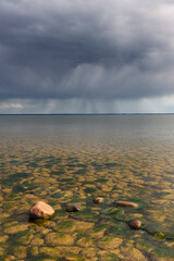 Dark clouds gather over Lake Vänern in Sweden, hinting at an impending storm and a tranquil landscape beneath the ominous skies