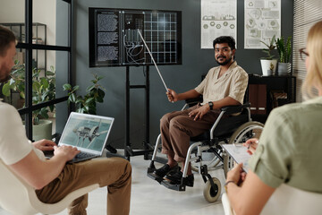 Confident architect with disability sitting in wheelchair and making presentation of solar panel to colleagues