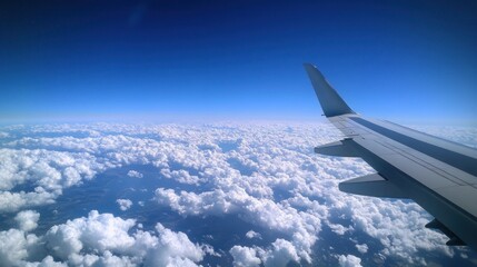 Obraz premium Aerial view from an airplane wing above fluffy clouds and a clear blue sky.