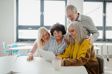 Group of senior students looking at tablet screen, learning new skill. Elderly people attending computer and technology education class. Digital literacy.