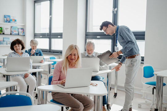 Teacher explaining senior students how to work with laptop and internet. Elderly people attending computer and technology education class. Digital literacy.