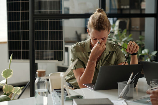 Young overworked female engineer bending over laptop while working late over new green energy project