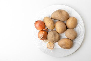 A white plate with fresh potatoes, onions, and garlic, ideal ingredients for traditional Thanksgiving dinner preparations