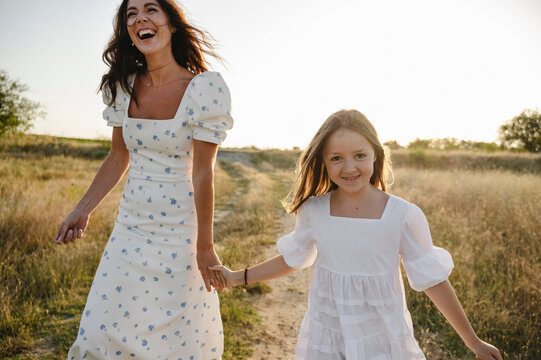 Cheerful mother holding hands with daughter and walking on field