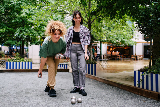 Happy young lesbian couple playing bocce balls in front of trees
