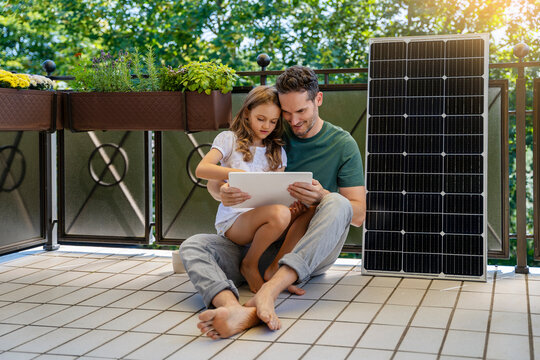 Daughter using tablet PC with father sitting next to solar panel in balcony - Powered by Adobe