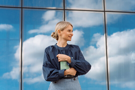 Smiling mature businesswoman with diary standing in front of glass wall