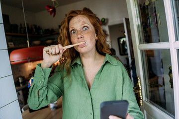 Freckled woman brushing teeth at home