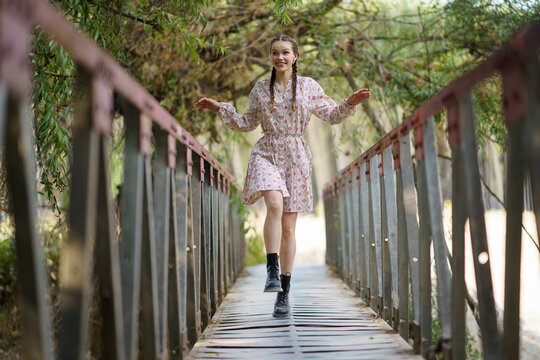 Happy young woman walking on bridge in front of trees