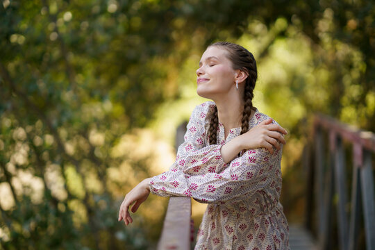 Happy woman standing with eyes closed in front of trees on bridge