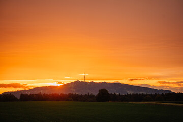 Fototapeta premium Golden sunset over a distant hill with a communication tower, casting a warm glow over the landscape with dark trees in the foreground..