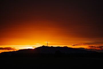 A striking sunset with deep orange hues behind a silhouette of hills and a tall communication tower on the horizon..