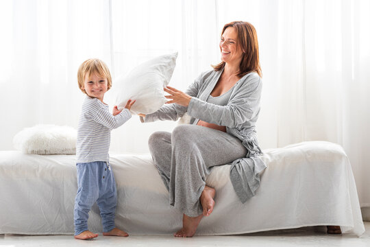 Happy mother and son playing with pillow at home