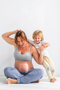 Pregnant woman playing with son near white wall