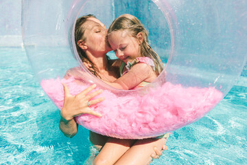 Happy mother kissing daughter and holding inflatable ring in swimming pool