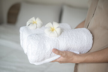 Hands of hotel maid putting plumeria flower and towels on the bed in the luxury hotel room ready for tourist travel