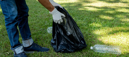 Hand holding plastic bottle waste, picking up trash and putting it in the black garbage bag at the...