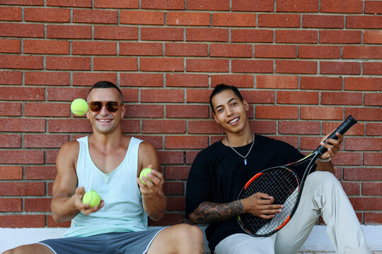 Happy siblings spending leisure time with tennis racket and ball near brick wall