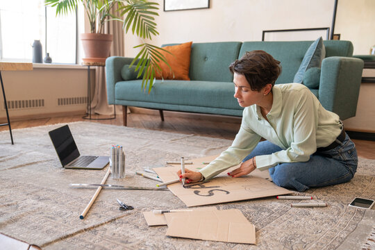 Activist making environment placard on carpet in living room at home