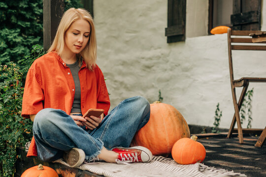 Blond woman using smart phone sitting cross-legged on porch