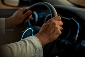 Hands of man holding steering wheel of car