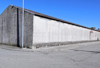 Fototapeta premium Old concrete industrial building at the roadside. Cement sidewalk and street in front. Background for copy space