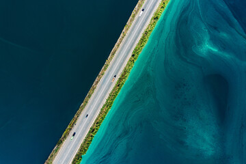 Aerial view of asphalt bridge road with cars and truck cargo between blue and turquoise water river sea ocean.