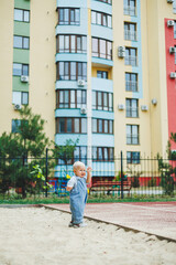 Obraz premium A toddler boy in denim overalls runs and plays on the playground. Active time of the child outside. A child runs on the street in the summer.