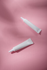 Two white narrow unbranded cosmetics tubes mockup on pink background. Beauty product template, advertising banner. Copy space, top view, flat lay