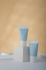 Blue Cosmetics tube mockup on concrete cube stand, yellow background. Unbranded beauty container, no label template. Product advertising banner, copy space