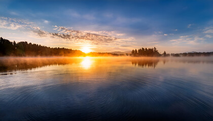 Fototapeta premium Stunning Sunrise Over Peaceful Lake and Scenic Forest. A breathtaking sunrise casts warm light over a tranquil lake and surrounding forest, creating a serene and vibrant atmosphere