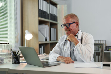 Obraz premium Male doctor, scientist, specialist working with laptop, making work calls, studying data, biological research at desk in office in hospital, clinic.