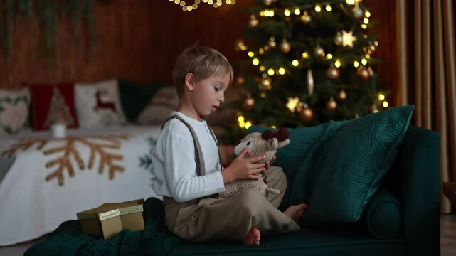 Sweet blond child, cute boy, playing with christmas toys on Christmas, beautifully decorated home for Christmas, cosy place