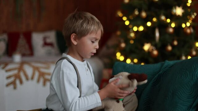 Sweet blond child, cute boy, playing with christmas toys on Christmas, beautifully decorated home for Christmas, cosy place