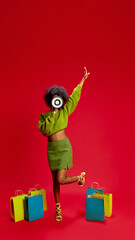 Naklejka premium Woman joyfully raises hand shouting to megaphone strikes playful pose with shopping bags. Excitement for sale or retail event. Concept of sale, celebration, retail, excitement, shopping, announcement