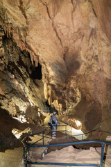 A man in a camouflage outfit is walking through a cave. The cave is dark and has a damp, earthy smell. The man is holding a backpack and he is exploring the cave.