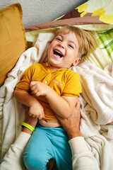 A joyful child laughs as his father tickles him on the bed, creating a fun and heartwarming family...