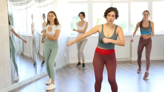 Expressive cheerful young Latina leading upbeat Zumba class for group of women in mirrored dance studio. High quality 4k footage